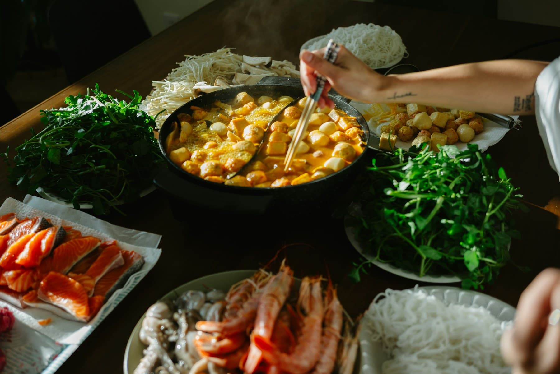 一桌摆满蔬菜、海鲜和肉类的火锅食材,中间锅底正在煮沸